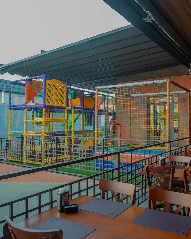 Varanda coberta com mesas e o espaço kids ao fundo